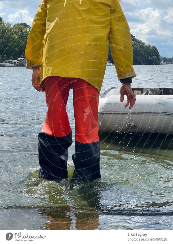 Mann mit Regenkleidung im Wasser Ein Mann allein Außenaufnahme Wassertropfen Wasseroberfläche Schlauchboot schwarzrotgelb Wasserwirbel einzeln 1 Mensch