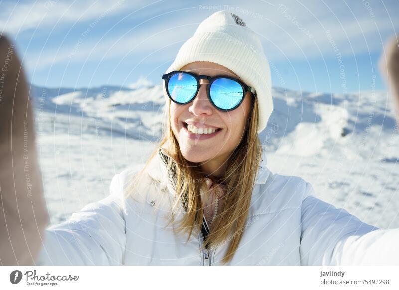 Fröhliche Frau mit Sonnenbrille nimmt Selfie in verschneiten Ort Winter Berge u. Gebirge Schnee kalt Lächeln Berghang fotografieren Abenteuer jung