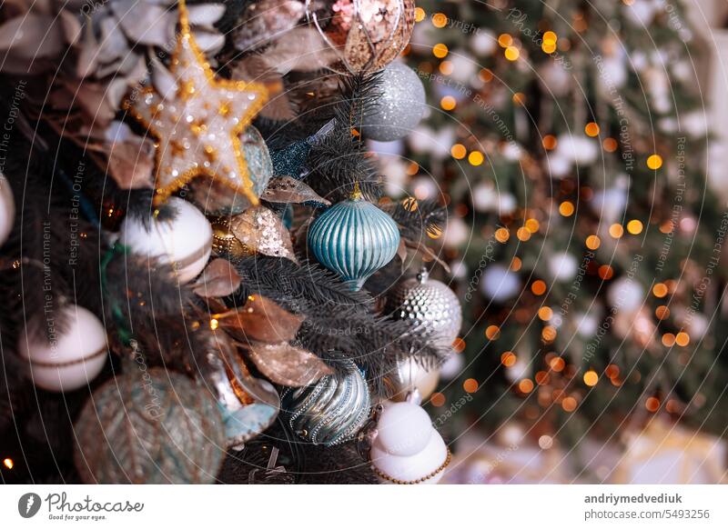 Nahaufnahme von Glamour Tannenzweige mit glänzenden silbernen und blauen Kugel oder Ball, Stern, Weihnachten Ornament und Lichter in dekorierten Wohnzimmer dekoriert. Weihnachtsferien Hintergrund. Festliche neue 2024 Jahr