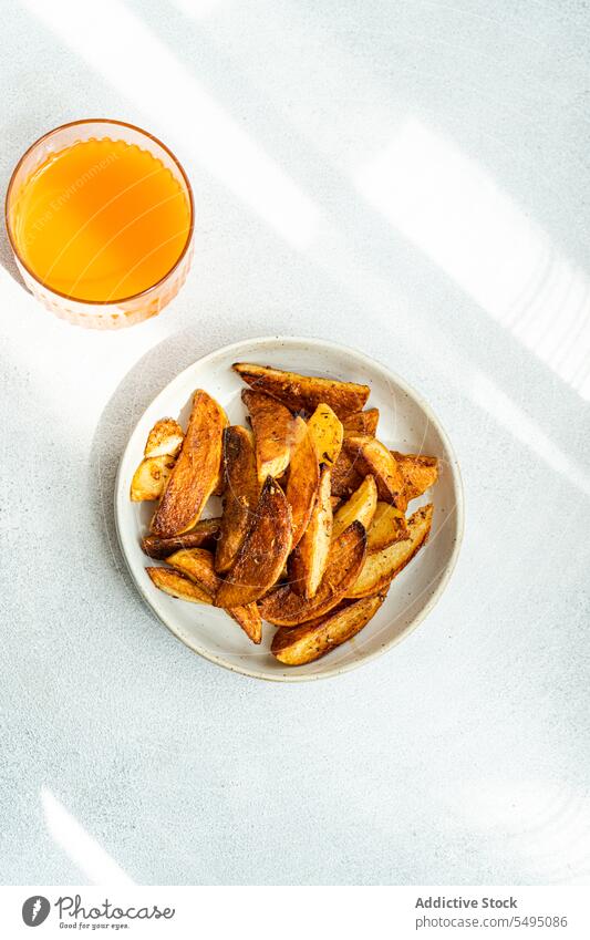 Gebratene Kartoffel mit Paprikagewürz, serviert auf einem Keramikteller neben Orangensaft gebraten Gewürz orange Saft Lebensmittel trinken Glas Tisch Teller