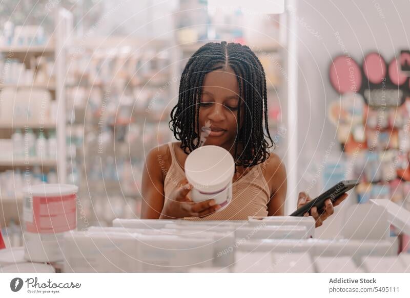 Schwarze Frau liest Informationen auf einer Medikamentenflasche und hält ein Smartphone in einem Geschäft Flasche lesen kaufen Kunde Apotheke Drogerie