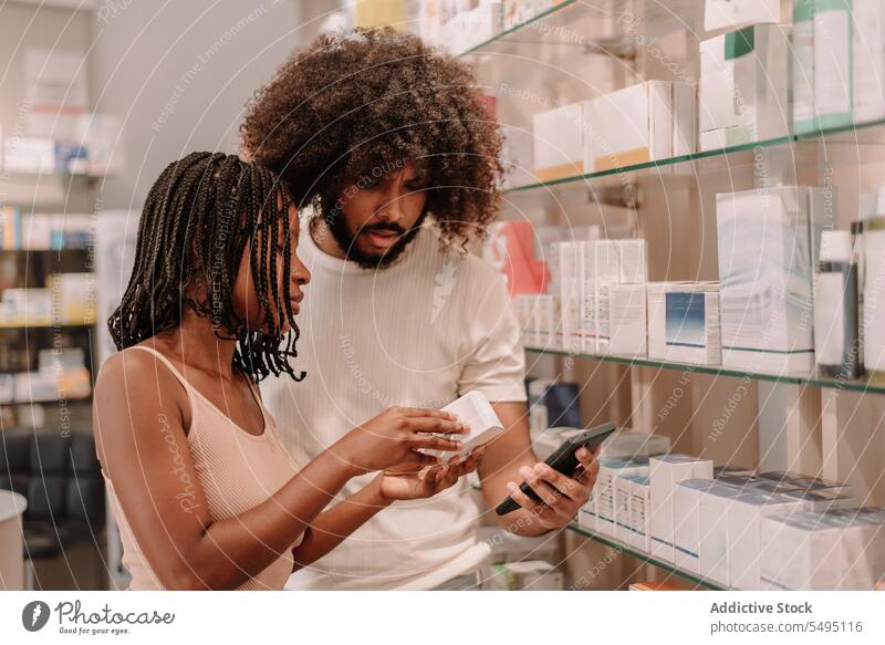 Schwarzes Paar liest in der Drogerie Informationen auf dem Handy Freund Freundin Funktelefon Apotheke kaufen Laden Mann Frau lesen Smartphone Medizin Flasche