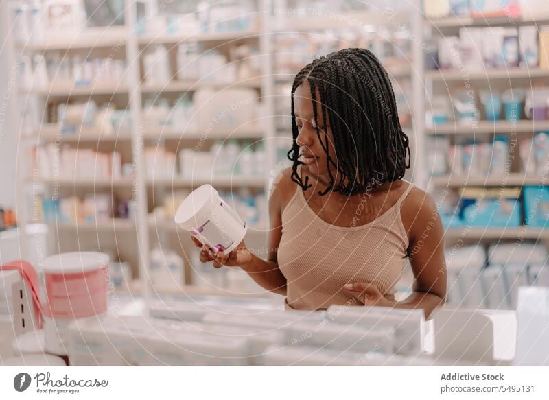 Schwarze Frau liest in einem Geschäft Informationen auf einer Arzneimittelflasche Flasche lesen kaufen Kunde Apotheke Drogerie selbstbewusst jung Produkt Klient