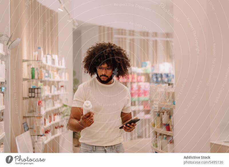 Schwarzer junger Mann hält Smartphone und liest Produktinformationen von der Medikamentenflasche in einem Apothekengeschäft Flasche lesen kaufen Information