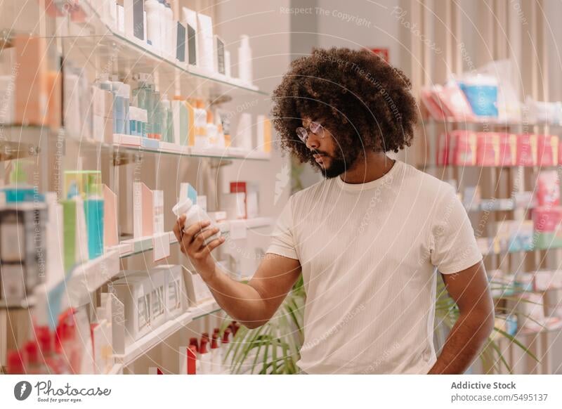 Schwarzer Mann mit Afrofrisur liest Etikett auf Flasche in Apotheke lesen kennzeichnen Bestandteil Medizin Drogerie kaufen Kunde Medikament Paket
