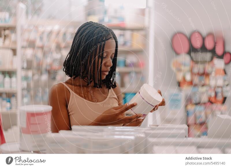 Schwarze Frau liest in einem Geschäft Informationen auf einer Arzneimittelflasche Flasche lesen kaufen Kunde Apotheke Drogerie selbstbewusst jung Produkt Klient