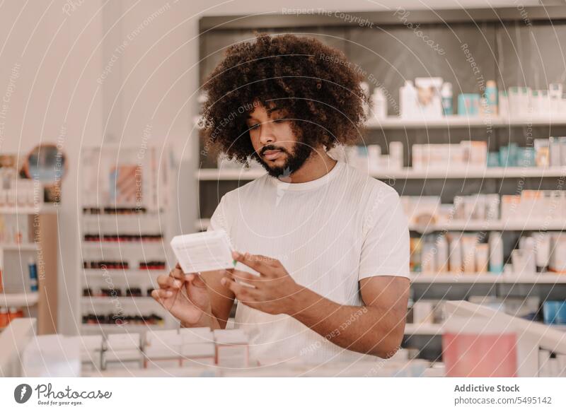 Afroamerikanischer Mann mit Afrohaar liest in der Apotheke das Etikett eines verschriebenen Medikaments lesen kaufen Information Medizin Kunde Verschreibung