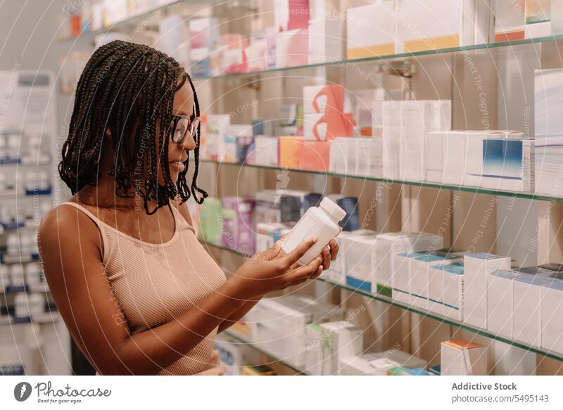 Schwarze Frau mit Dreadlocks liest in der Apotheke das Etikett auf der Flasche lesen kennzeichnen Bestandteil Medizin Drogerie kaufen Kunde Medikament Paket