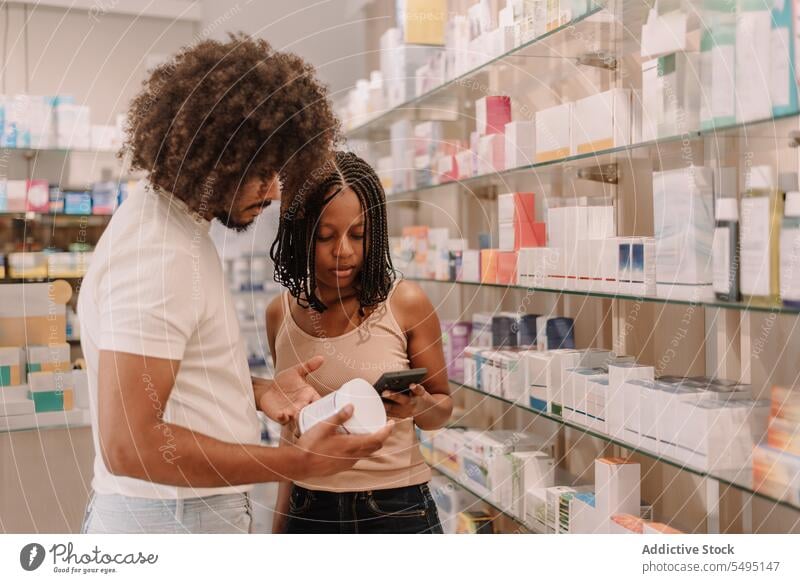 Schwarzes Paar liest in der Drogerie Informationen auf dem Handy Freund Freundin Funktelefon Apotheke kaufen Laden Mann Frau lesen Smartphone Medizin Flasche