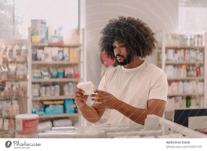 Afroamerikanischer Mann mit Afrohaar liest in der Apotheke das Etikett eines verschriebenen Medikaments lesen kaufen Information Medizin Kunde Verschreibung