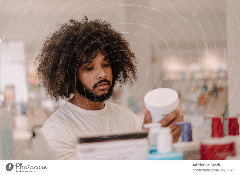 Schwarzer Mann liest in der Apotheke die Inhaltsstoffe auf der Medikamentenflasche lesen Bestandteil Flasche Drogerie kennzeichnen Kunde kaufen Medizin
