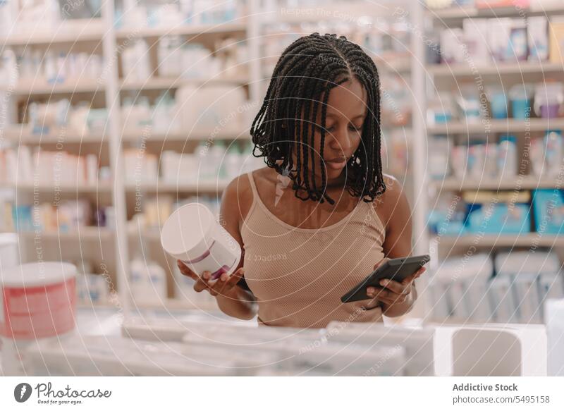 Schwarze Frau mit Medikamentenflasche liest im Geschäft Informationen auf dem Smartphone Flasche lesen kaufen Kunde Apotheke Drogerie selbstbewusst jung online