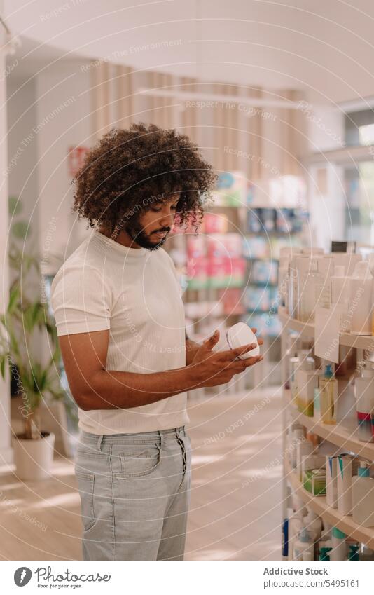 Schwarzer Mann mit Afrofrisur liest Etikett auf Flasche in Apotheke lesen kennzeichnen Bestandteil Medizin Drogerie kaufen Kunde Medikament Paket