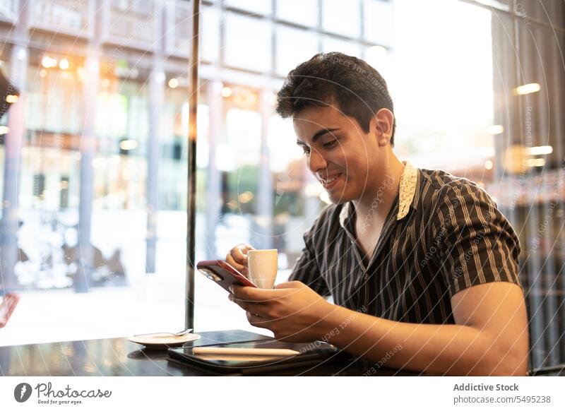 Mann hält Kaffeetasse und benutzt Smartphone in Cafés Tasse benutzend Lächeln jung Sitzen Fenster digital Tablette Lifestyle Mobile Telefon Heißgetränk