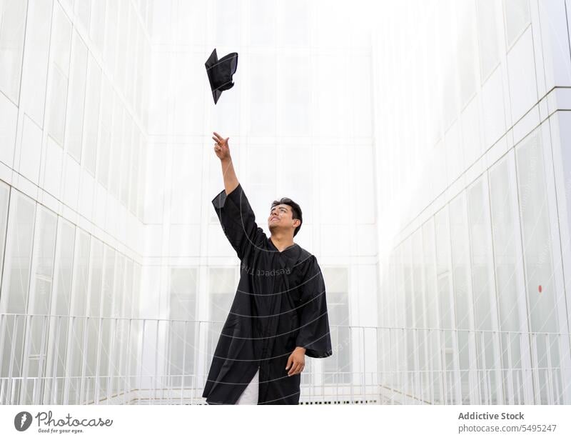 Mann in Graduierungsrobe wirft Mörtelbrett in die Luft Schüler Abschluss Kleid Verschlussdeckel Werfen in der Luft heiter Bildung Errungenschaft Glück schwarz