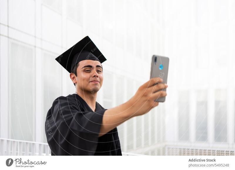 Mann in Abschlussrobe und Kappe macht Selfie über Telefon Kleid Mörtelbrett Smartphone Schüler Apparatur Errungenschaft Lächeln gutaussehend Mobile
