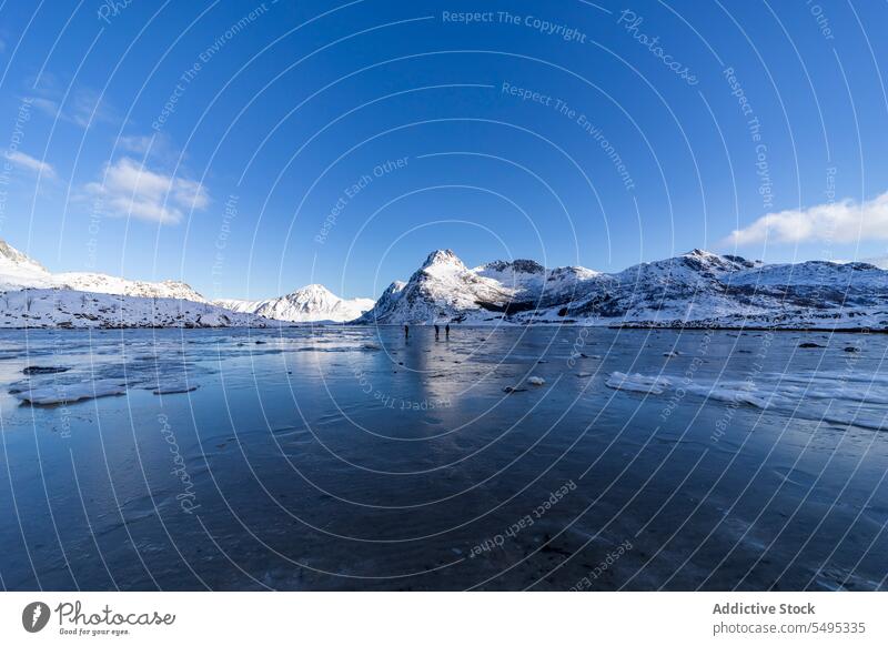 Reisende stehen auf einem zugefrorenen See in der Nähe verschneiter Berge Reisender Tourist Berge u. Gebirge Winter Schnee Natur lofoten Insel Norwegen Ufer