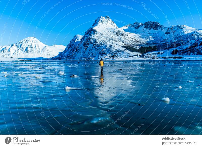 Reisender auf zugefrorenem See in der Nähe verschneiter Berge Tourist Berge u. Gebirge Winter Schnee Natur lofoten Insel Norwegen Ufer Küste kalt Blauer Himmel