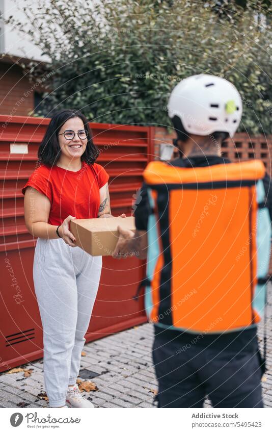 Zufriedener Kunde, der ein Paket vom Kurier auf dem Bürgersteig erhält Frau Auslieferer Empfang Karton Kasten Kollo Lächeln Dienst Versand behüten Mann