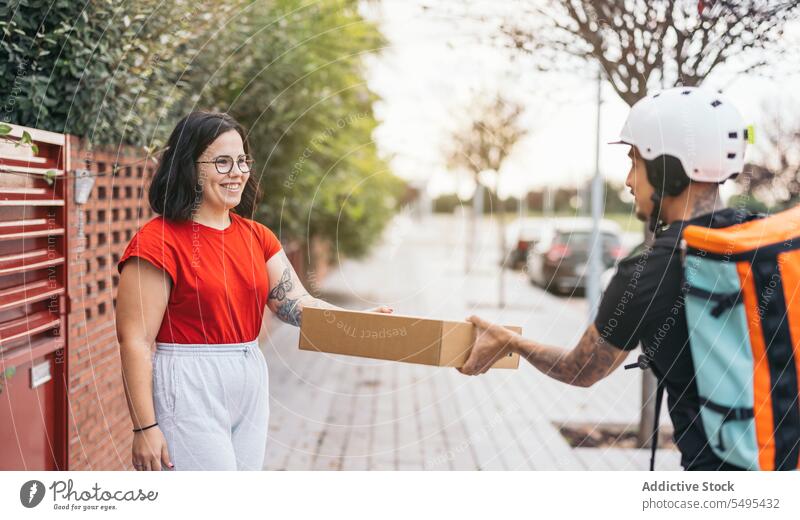 Zufriedener Kunde, der ein Paket vom Kurier auf dem Bürgersteig erhält Frau Auslieferer Empfang Karton Kasten Kollo Lächeln Dienst Versand behüten Mann