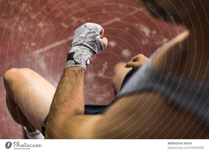Crop unerkennbar Boxen Mann sitzt mit gewickelten Hand mit Klebeband im Tageslicht Athlet Boxer umhüllen Training Sport Kämpfer üben männlich Sportler