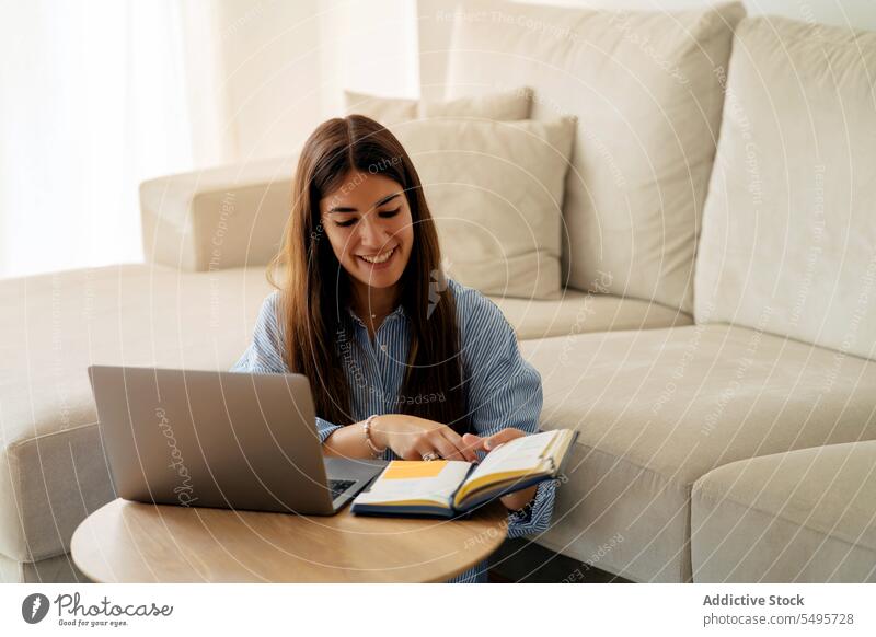 Lächelnde Frau arbeitet an einem Laptop im Wohnzimmer Unternehmer freiberuflich Arbeit lesen Planer heimwärts abgelegen jung Job positiv Notebook Gerät Hinweis