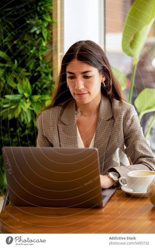 Frau sitzt am Tisch mit Kaffeetasse und arbeitet am Laptop freiberuflich abgelegen Internet Inbetriebnahme Arbeit Arbeitsplatz Café online Browsen Surfen