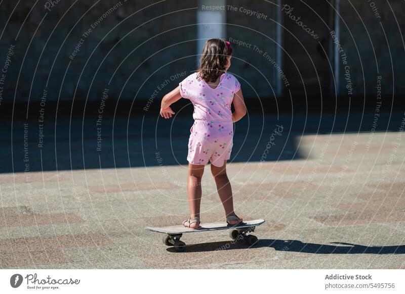 Kleines Mädchen fährt Longboard auf sonniger Straße Mitfahrgelegenheit Skater Kind Großstadt Sommer Aktivität Hobby lässig Lifestyle niedlich Straßenbelag