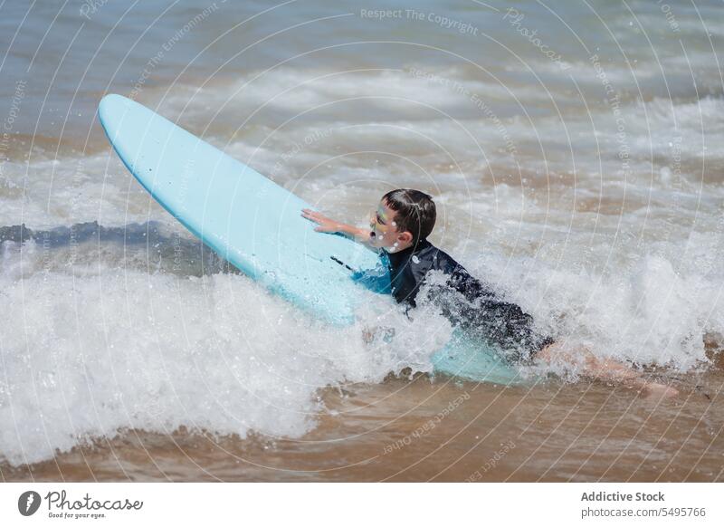 Kind mit Surfbrett im Meer Junge Surfer schwimmen MEER winken Lügen Surfen Sommer männlich Urlaub Meereslandschaft Natur Glück Zusammensein spielerisch Wasser