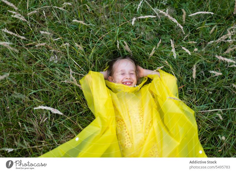 Kleines süßes Mädchen auf grünem Gras liegend Kind Lachen Natur Glück Lügen Wiese genießen Spaß haben spielen wenig Regenmantel Kindheit positiv Inhalt