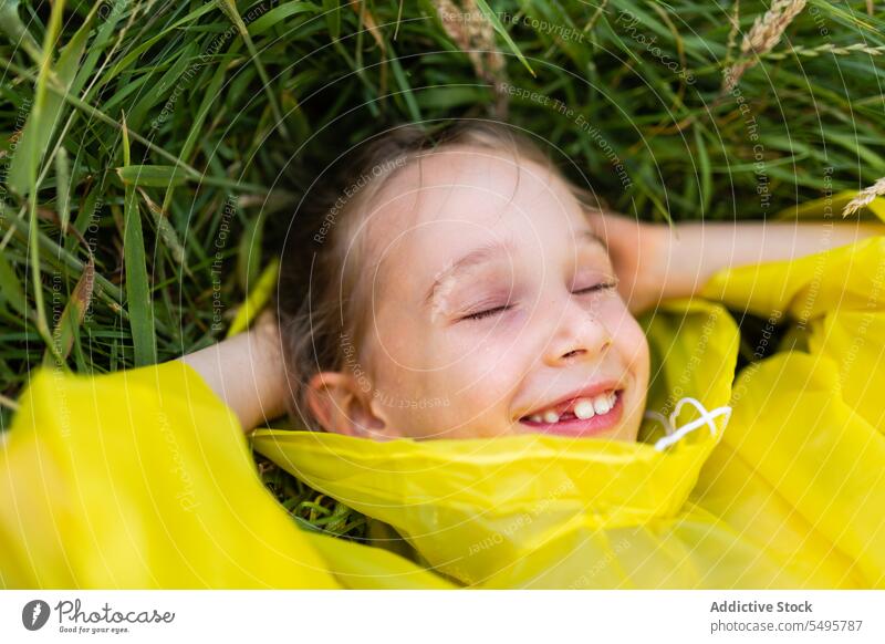 Kleines süßes Mädchen auf grünem Gras liegend Kind Lachen Natur Glück Lügen Wiese genießen Spaß haben spielen wenig Regenmantel Kindheit positiv Inhalt