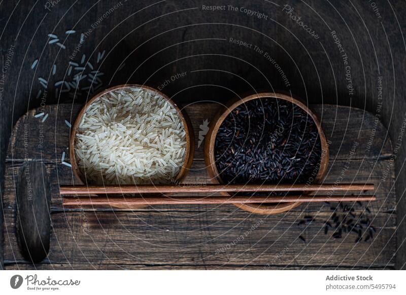 Roher schwarzer Wildreis und geschälter weißer Reis in den Schüsseln mit Stäbchen. roh wild Schalen & Schüsseln Essstäbchen Tisch Oberfläche Lebensmittel