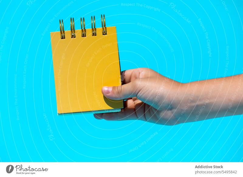 Crop-Hand mit Spiral-Notizbuch in blauem Studio Notebook Notizblock Spirale hell blanko Attrappe Halt zeigen manifestieren Konzept pulsierend Bildung Papier
