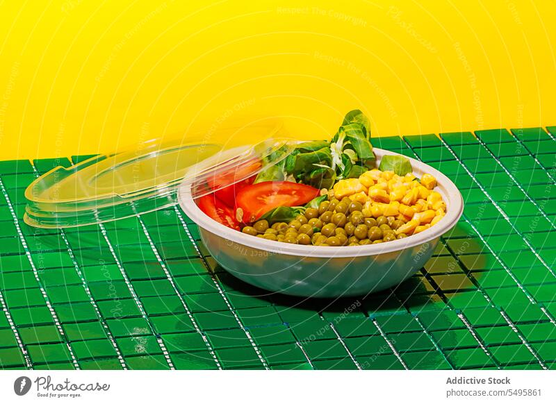 Salatschüssel auf grünem Hintergrund mit Plastikdeckel vor gelber Wand Schalen & Schüsseln Salatbeilage Lebensmittel Scheibe Tomate Spinat Blatt Mais Kernel