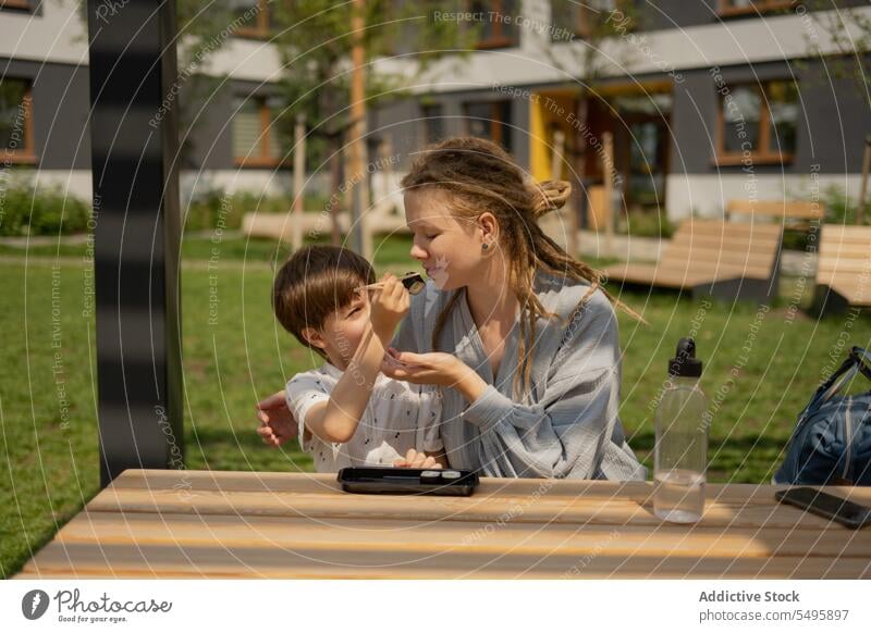 Junge füttert Frau im Sommer im Park mit Sushi Mutter Sohn füttern Tisch Familie Lebensmittel teilen Liebe Rastalocken Lifestyle Picknick wenig Essstäbchen