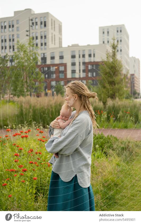 Frau trägt und küsst Baby im Park gegen den Himmel Mutter tragen Kopf Liebe klein Umarmung bezaubernd Familie Lifestyle niedlich Rastalocken Säugling