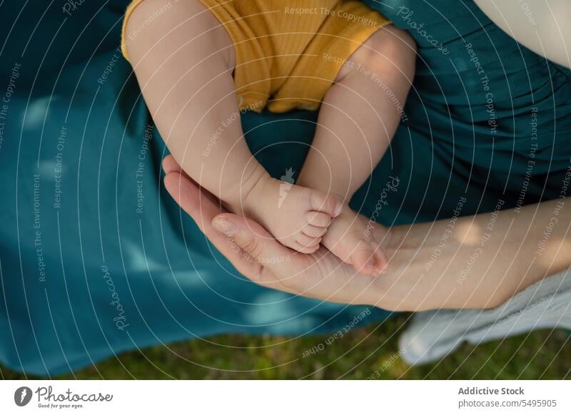 Die Hand der Mutter hält die Beine des Babys, während sie im Park sitzt Frau Beteiligung Ernte Familie Angebot Liebe Körperteil Zusammensein Säugling Wochenende