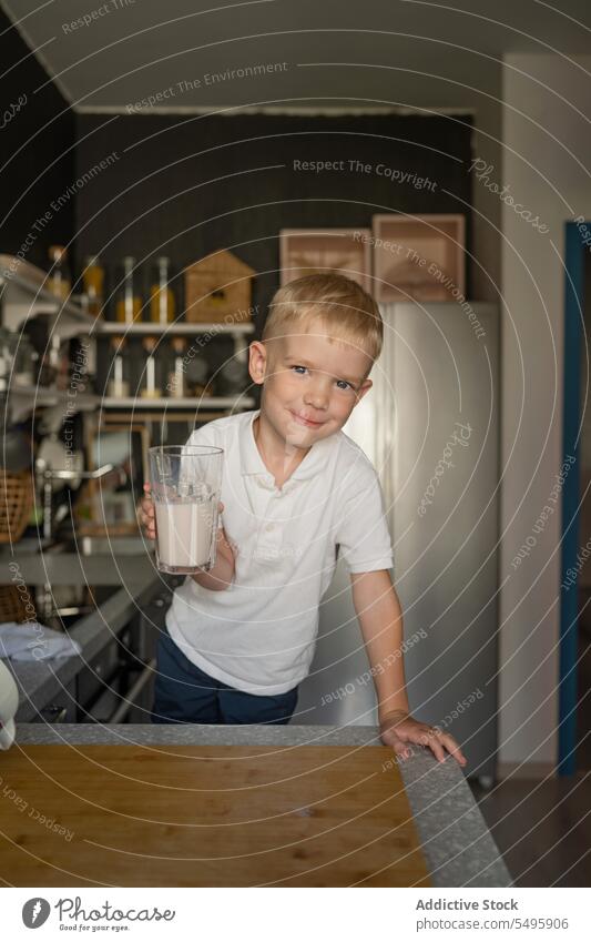 Lächelnder Junge, der ein Milchglas hält und in der Küche steht melken Glas Koch niedlich Beteiligung Lebensmittel Arbeitsplatte trinken Gesundheit blondes Haar