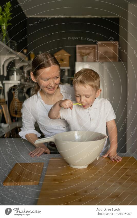 Glückliche Mutter betrachtet ihren Sohn beim Probieren von Essen in der Küche Verkostung Lebensmittel Lächeln Essen zubereiten Frau Junge Familie Blick Löffel