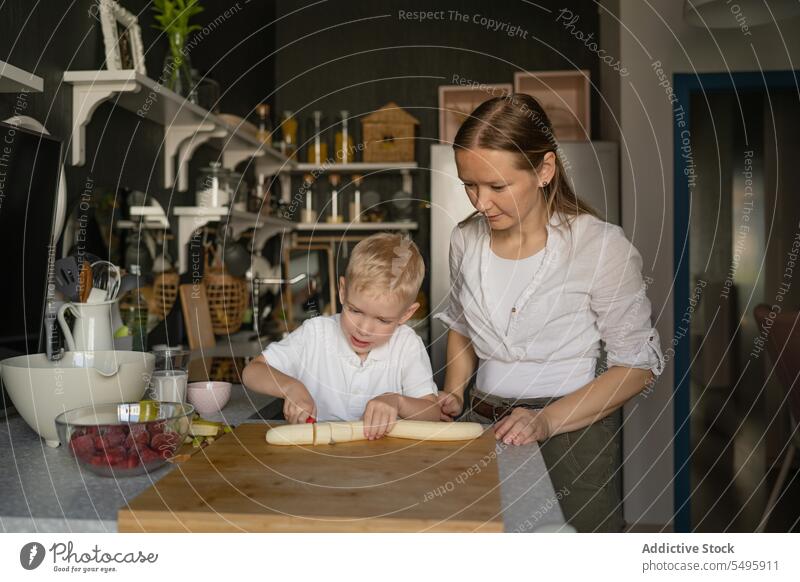 Frau sieht Junge beim Schneiden von Bananen auf einem Brett in der Küche an Mutter Sohn Koch Zusammensein Frucht vorbereiten Lebensmittel Familie Kind Messer