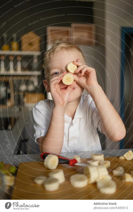 Junge hält sich in der Küche Bananenscheiben vor das Gesicht Scheibe Beteiligung Koch Kind vorbereiten niedlich spielerisch Spielfigur Schneiden Frucht