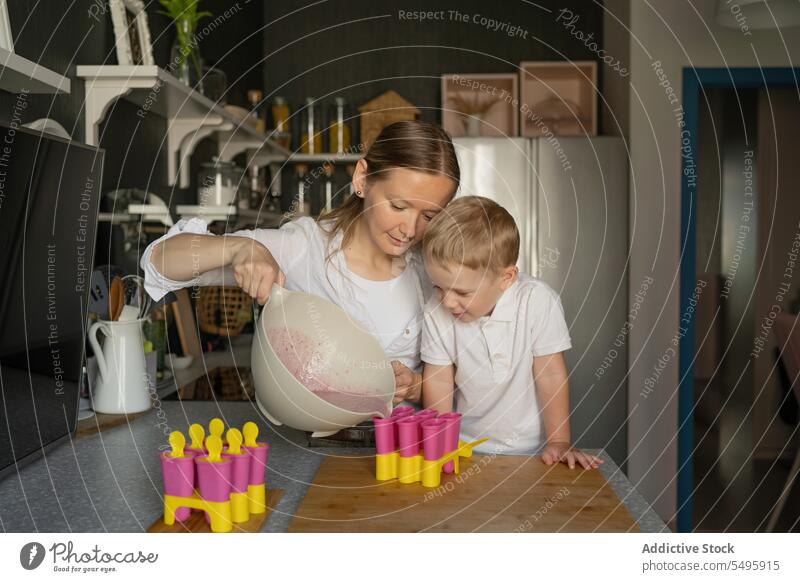 Junge sieht Frau bei der Eisherstellung in der Küche zu Mutter Sohn Gießen Speiseeis liquide Herstellung Stieleis gegossen blondes Haar Familie neugierig Blick