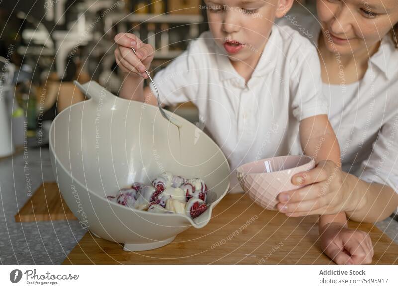 Junge und Mutter mischen Kondensmilch und Erdbeeren in einer Schüssel Frau Mischen Schalen & Schüsseln Löffel Essen zubereiten Dame Küche Kind süß Lebensmittel