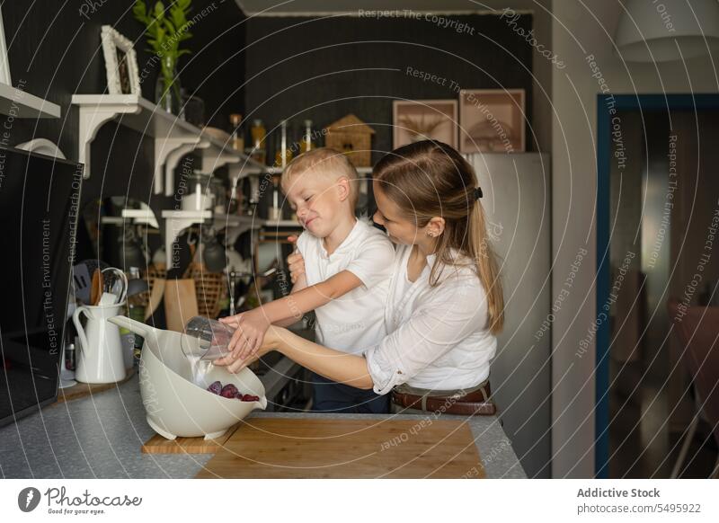 Frau und Junge gießen Milch in eine Schüssel in der Küche Mutter Sohn Gießen melken Schalen & Schüsseln Erdbeeren Essen zubereiten Familie Frucht Brille Lächeln