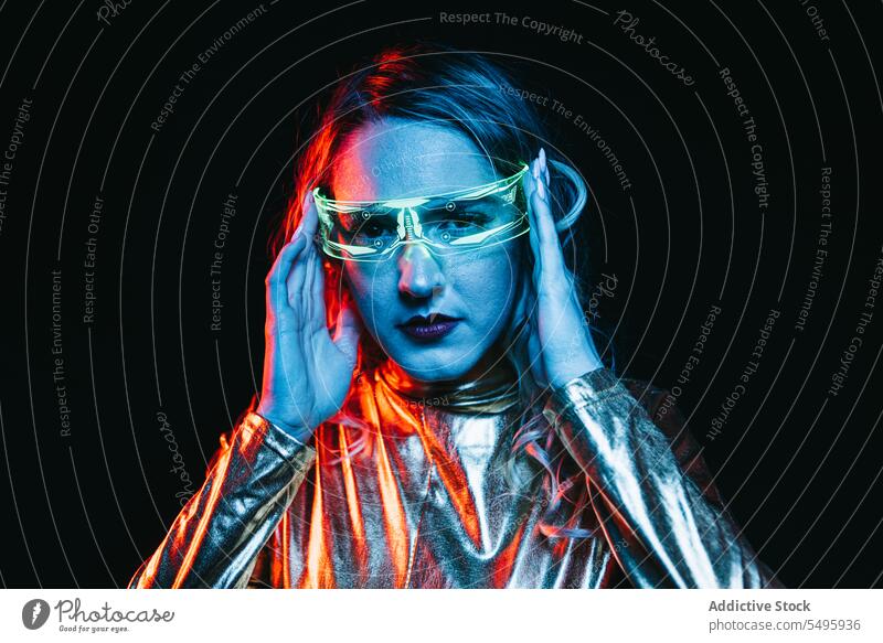 Kybernetisches junges Mädchen vor dunklem Hintergrund kybernetisch lockig Behaarung blond Brille futuristisch anhaben hell reflektierend Bekleidung