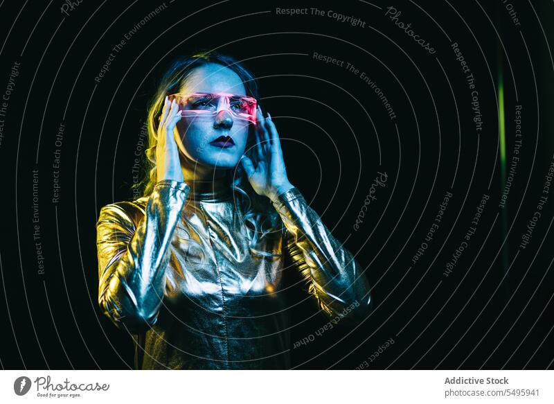 Kybernetisches junges Mädchen vor dunklem Hintergrund kybernetisch lockig Behaarung blond Brille futuristisch anhaben hell reflektierend Bekleidung emotionslos