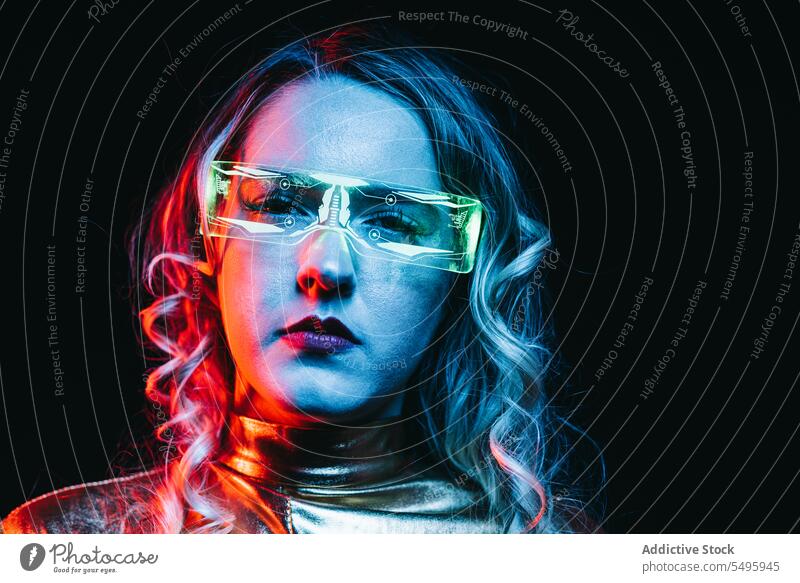 Kybernetisches junges Mädchen vor dunklem Hintergrund kybernetisch lockig Behaarung blond Brille futuristisch anhaben hell reflektierend Bekleidung