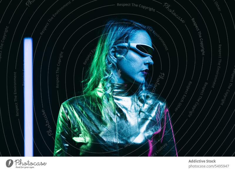 Kybernetisches junges Mädchen vor dunklem Hintergrund mit Lichtern kybernetisch lockig Behaarung blond Brille futuristisch anhaben hell reflektierend Bekleidung