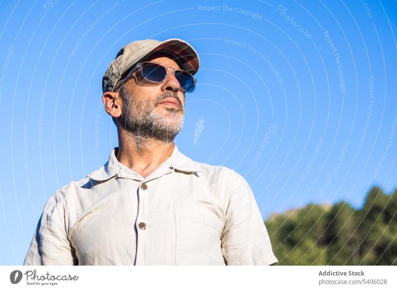 Selbstbewusster bärtiger Mann mit Sonnenbrille und Mütze selbstbewusst Sommer Blauer Himmel Verschlussdeckel ernst Vollbart brutal Vorschein männlich unrasiert