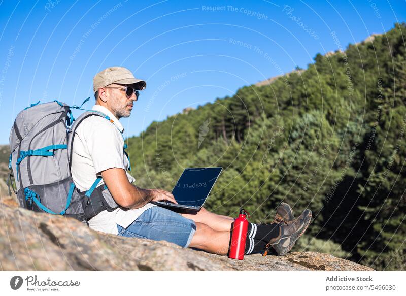 Älterer Reisender mit Laptop auf felsiger Klippe Mann freiberuflich Arbeit Natur Browsen Felsen benutzend männlich Pflanze abgelegen Apparatur Sommer Gerät